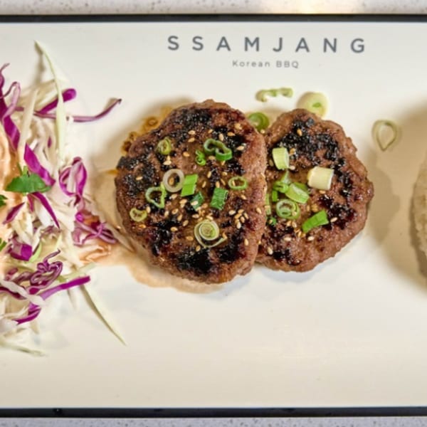 Two grilled Korean BBQ patties with green onions and sesame seeds, served with coleslaw.