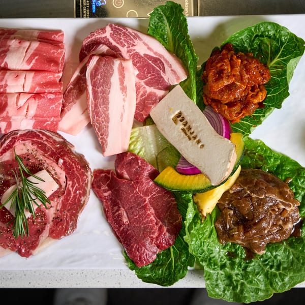 A platter of various raw Korean BBQ meats, including marinated and unmarinated cuts, with lettuce and vegetables.