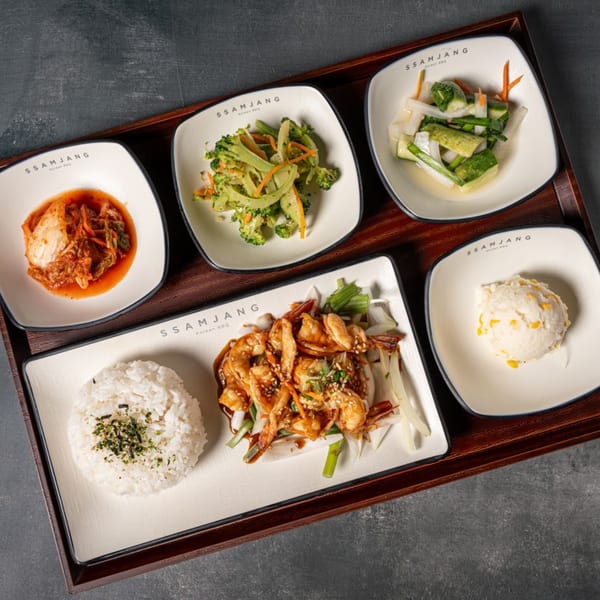 A Korean BBQ meal with shrimp, rice, kimchi, broccoli, pickled vegetables, and corn salad on a tray.