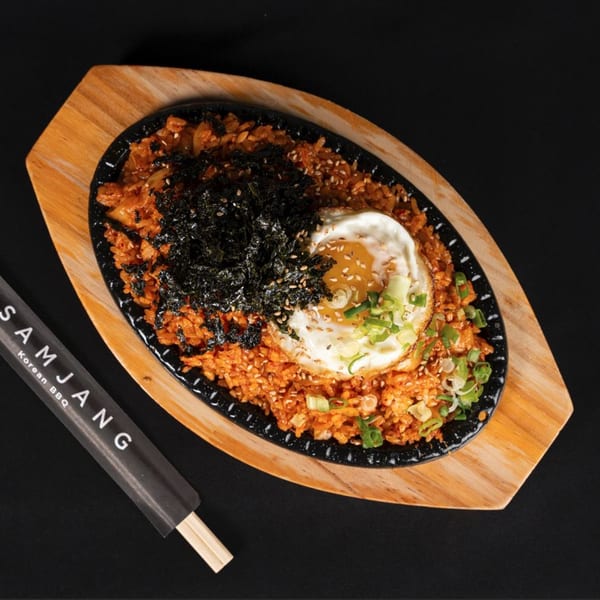 Kimchi fried rice with a fried egg, seaweed, and green onions on a black skillet.