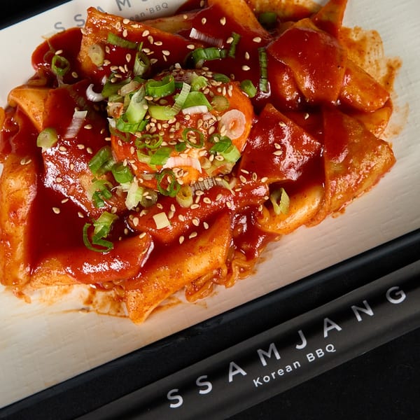 Spicy Korean Tteokbokki with a boiled egg, green onions, and sesame seeds, served on a white plate.