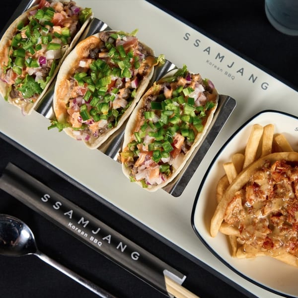 Three Korean BBQ tacos with green peppers and a side of loaded fries on a white tray.