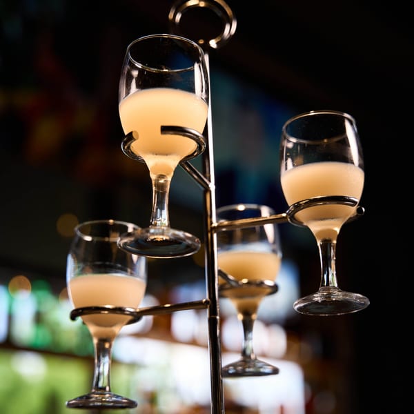 Four glasses of creamy Korean rice wine, Makgeolli, displayed on a metal stand.