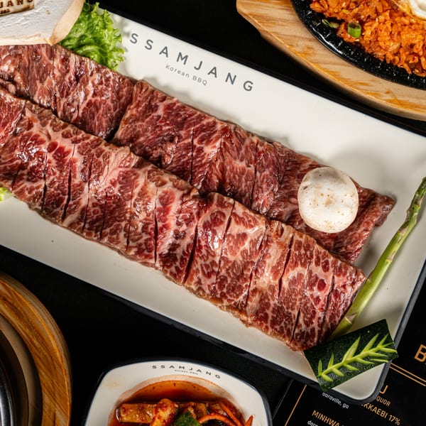 Raw, marbled Korean BBQ short ribs on a white platter with a mushroom and asparagus.