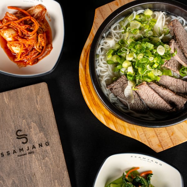 Korean BBQ meal with beef noodle soup, kimchi, and a side dish on a black table.