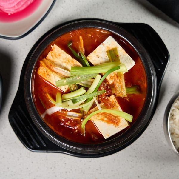 A black stone bowl of SSAMJANG Korean BBQ kimchi jjigae with tofu and green onions.