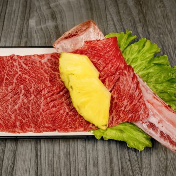 Raw Korean BBQ beef ribs and sliced pineapple on lettuce, ready for grilling.