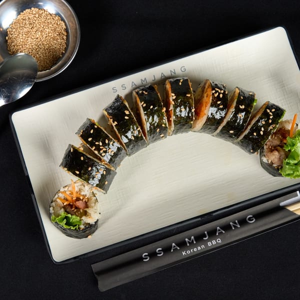 Sliced Korean BBQ kimbap with sesame seeds on a white plate, with chopsticks and sesame seeds.