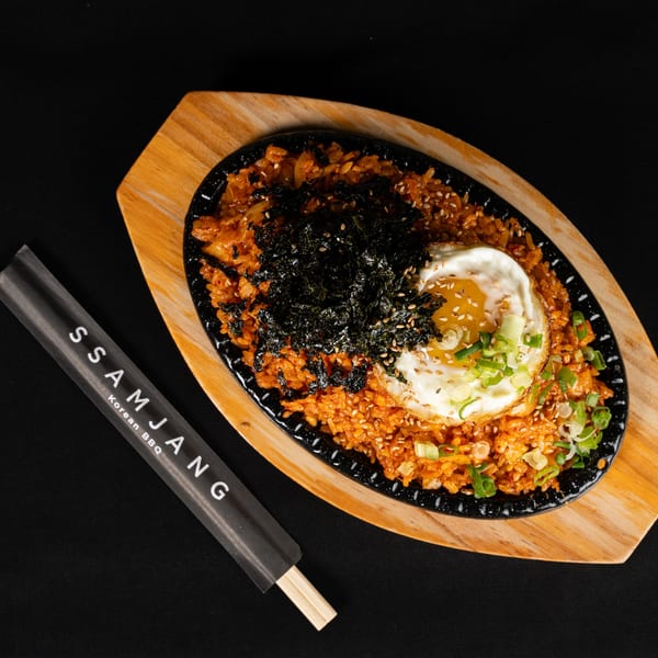 Kimchi fried rice with a fried egg, seaweed, sesame seeds, and green onions, served on a black skillet.