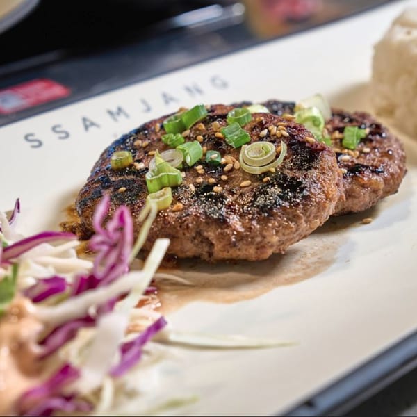 Two Korean BBQ patties topped with green onions and sesame seeds, with a side of coleslaw.