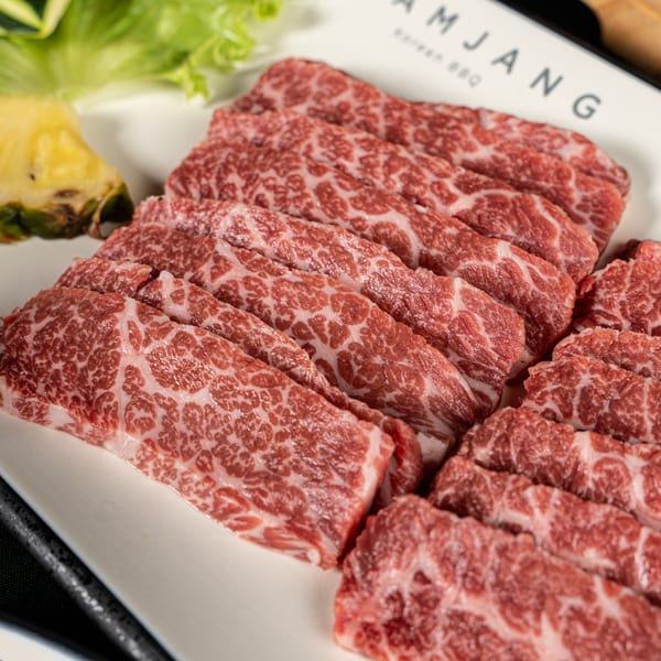 Marbled raw beef slices, pineapple, and lettuce on a white plate from SSAMJANG Korean BBQ.