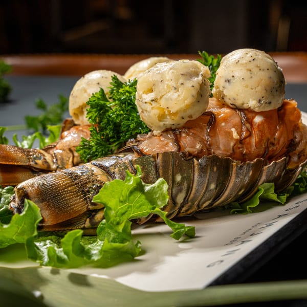 Grilled lobster tail topped with scoops of butter and fresh parsley, served on lettuce.