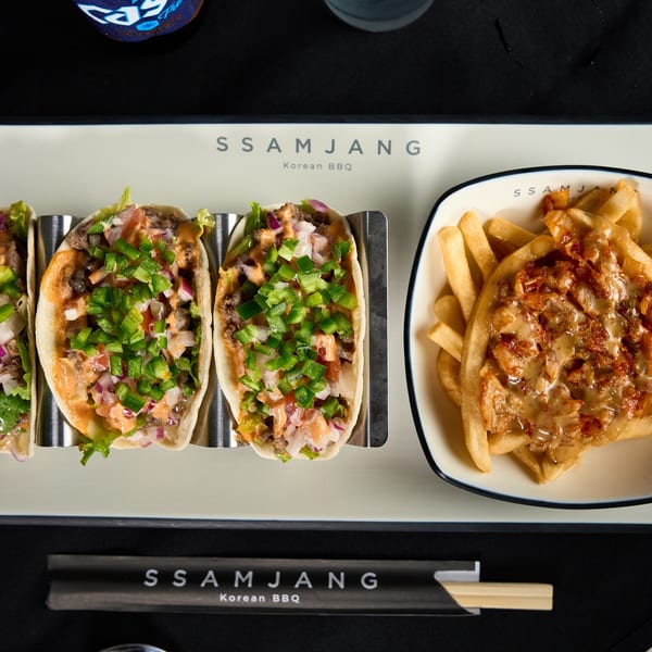 Three Korean BBQ tacos with green peppers and a side of cheesy fries on a branded tray.