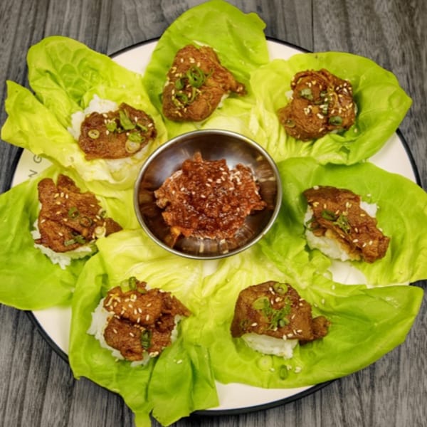 Korean BBQ lettuce wraps with grilled meat, rice, sesame seeds, green onions, and a dipping sauce.