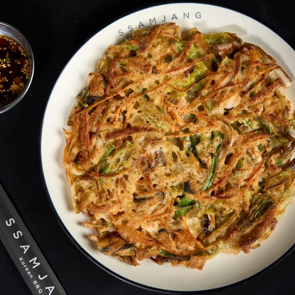 A crispy Korean seafood pancake (Haemul Pajeon) with dipping sauce on a black background.
