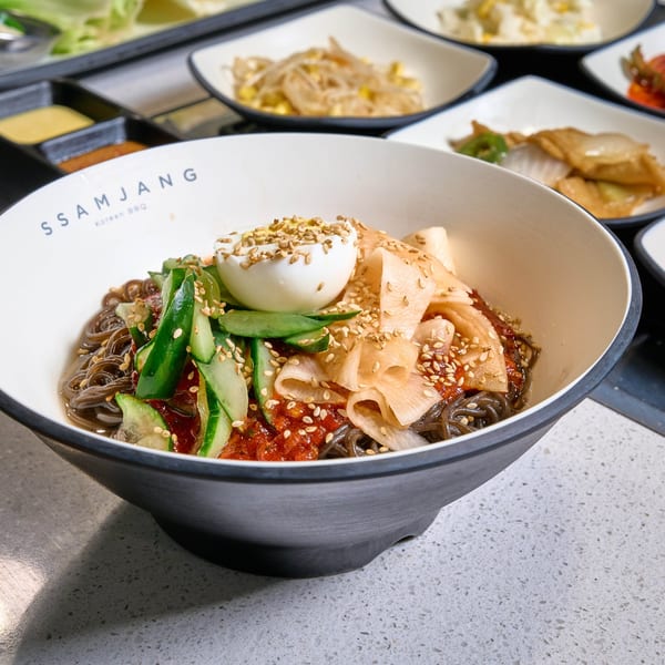 A bowl of SSAMJANG Korean BBQ cold noodles with cucumber, radish, egg, and sesame seeds.